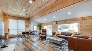 Un salón amplio con techo de madera, un conjunto de sofás, una mesa de centro y un comedor con mesa y sillas.