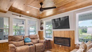 Una sala de estar con techo de madera, ventanas amplias, un televisor de pantalla plana y un sofá reclinable.