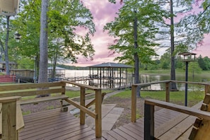 A wooden deck with benches overlooking a lake, a gazebo, and a dock with a boat.