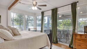 Un dormitorio con una cama grande, un ventilador de techo, un aparador de madera y vistas al exterior a través de amplias ventanas.