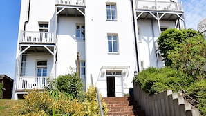 A white multi-story building with a central entrance, a small balcony on the ground floor, and a brick staircase leading up to the entrance. - Villa Hamburg Appartement 08 (Seebad Ahlbeck)