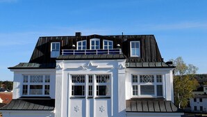 Uma casa de dois andares com telhado preto e paredes externas brancas.