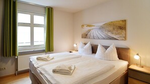 Een hotelkamer met een bed, twee nachtkastjes, gordijnen voor het raam, een radiator en een schilderij aan de muur.