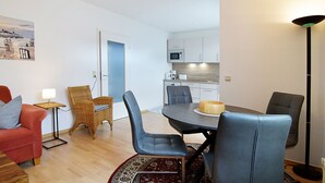 Een compacte woonruimte met een eethoek, kitchenette en een zithoek met een bank en stoelen.