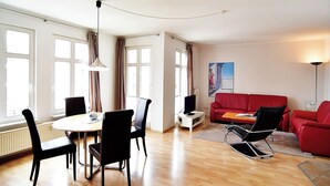 Ein Zimmer mit Esstisch, Stühlen, einem roten Sofa, einem Fernseher und einem Poster an der Wand.