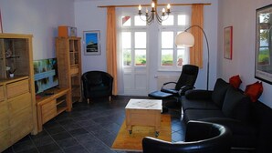 A living room with a television, wooden furniture, a black sofa, a coffee table, and a chandelier. - Villa Vineta Appartement 6/7 (Seebad Bansin)