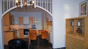 A modern kitchen with wooden cabinets, a dining area with orange chairs, and a black chair. - Villa Vineta Appartement 6/7 (Seebad Bansin)