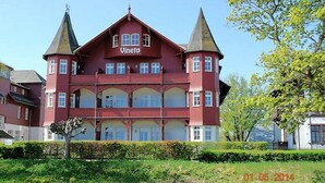 A red building with the name "Vineta" on the facade, featuring multiple balconies and a symmetrical design with two towers. - Villa Vineta Appartement 6/7 (Seebad Bansin)