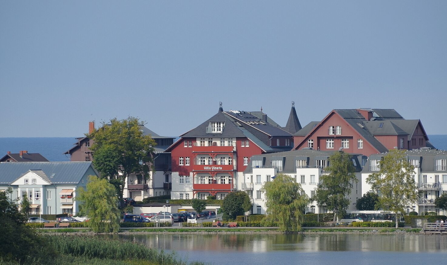 Et hotel ved søen med flere bygninger, heriblandt en markant rød bygning med teksten "Villa Vineta".