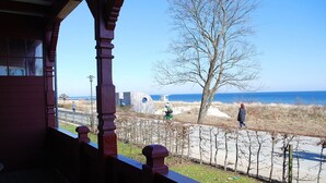 A coastal view from a building with a wooden balcony, a sandy path, and a person walking. - Villa Vineta Appartement 6/7 (Seebad Bansin)