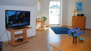Ein Wohnzimmer mit Fernseher, Holzmöbeln, einem blauen Teppich und einer Vase mit Blumen.