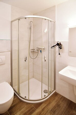 Een moderne badkamer met een douchecabine van glas, een witte wastafel en een toilet.