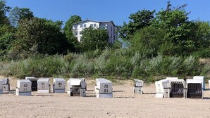 Una hilera de cabañas de playa numeradas en una playa arenosa, con un edificio al fondo.