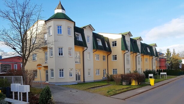 Ein mehrgeschossiges Wohngebäude mit symmetrischer Fassade, zahlreichen Fenstern und einem begrünten Dach.