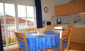 A dining area with a blue tablecloth, wooden chairs, and a basket. There is a window with a view of buildings outside.