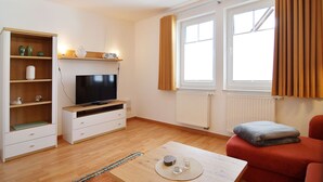 Een moderne woonkamer met een flatscreen televisie, houten planken, een rode bank en een groot raam met gordijnen.
