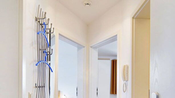 Een hal met een plafondlamp, een telefoon aan de muur en een rek met meerdere haken.