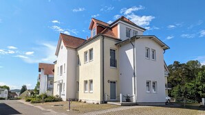 Een gebouw met twee verdiepingen, een witte gevel en een dak met rode dakpannen, met meerdere ramen en een hekwerkentree.