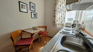 Een kleine kitchenette met een spoelbak, een magnetron en een koffiezetapparaat. Er staan twee stoelen bij een tafel met een placemat.