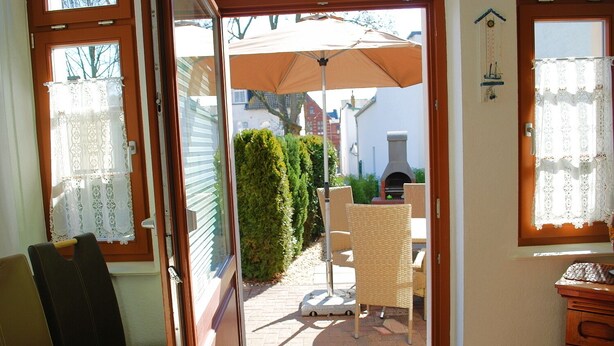 Una puerta que da a un patio al aire libre con una silla de mimbre, una mesa y un paraguas grande.