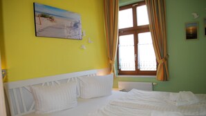 Una habitación de hotel con una cama, un cuadro en la pared y una ventana con cortinas.