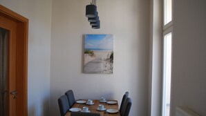 A dining area with a wooden table set for four, a painting of a beach scene, and a window providing natural light. - Villa Anna an der Ahlbecker Strandpromenade, App. 05 (Ostseebad Heringsdorf OT Ahlbeck)