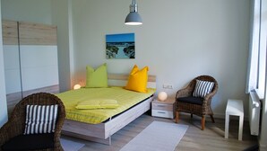 Una camera da letto con un letto, due poltrone in vimini, un comodino, una lampada e un quadro appeso al muro.