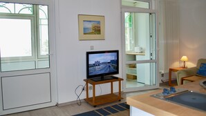 Een kamer met een televisie op een houten standaard, een schilderij aan de muur en uitzicht door een glazen deur.