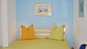 Een bed met gestreept beddengoed, twee kussens en een ingelijst foto aan de muur.