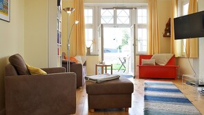 Ein Wohnzimmer mit einem braunen Sofa, einem roten Sofa, einem Couchtisch, einem Bücherregal, einer Stehlampe und einem Fernseher.