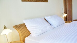 Ein ordentlich gemachtes Bett mit weißen Bettwäsche und zwei Kissen, daneben zwei Weidenholz-Nachttische mit Lampen.