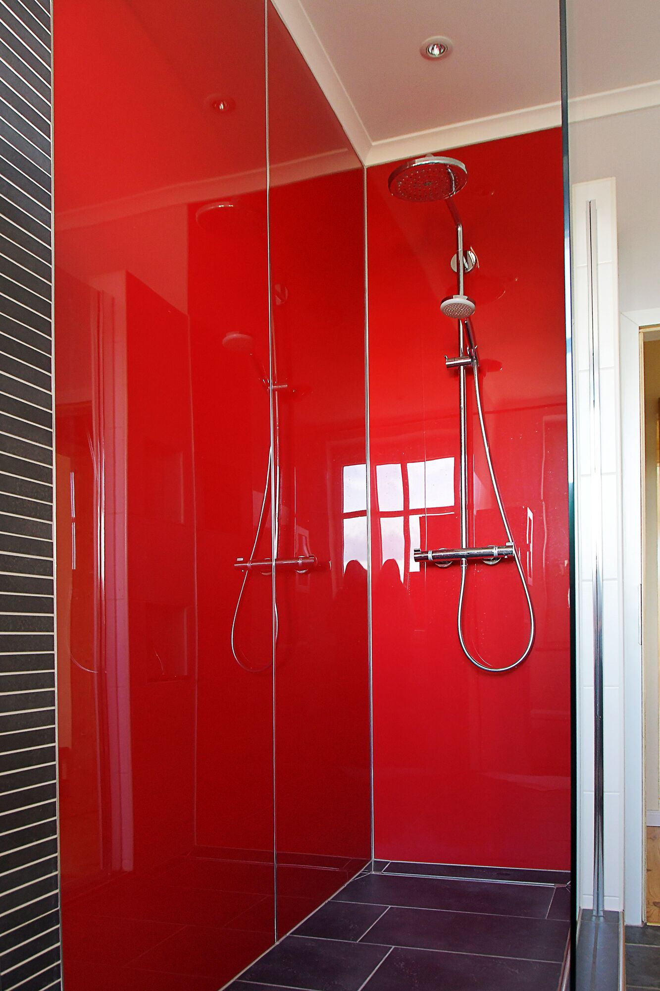 Une salle de bain moderne avec une douche à parois en verre rouge, un pommeau de douche à main et un robinet mural.