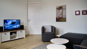 En stue med fjernsyn, sofa, lænestol og et lille bord.