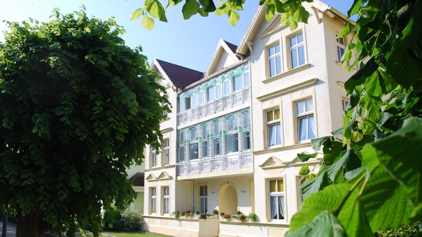 En bygning med flere etager, balkon, store vinduer og en velholdt græsplæne.