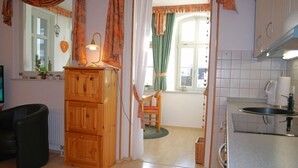Een gezellige woonkamer met een houten kast, een zwarte stoel en een raam met gordijnen.