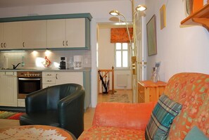 Un salon avec un canapé et un fauteuil, une cuisine avec des meubles blancs et un coin repas avec une table et des chaises.