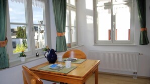 Een eetruimte met een houten tafel, twee stoelen, een vaas en een raam met gordijnen.