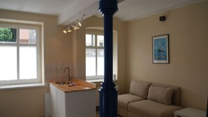 Una cocina moderna con encimera de madera, un lavamanos y un pilar azul. Hay un sofá beige y una pequeña mesa en la zona de estar.