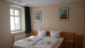 Una cama bien hecha con ropa de cama y toallas blancas, un cabecero de madera, una mesita de noche con una lámpara y dos cuadros enmarcados en la pared.