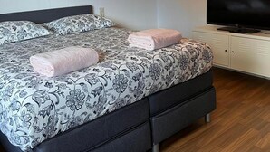 A neatly made bed with floral bedding, a television on a stand, and a white cabinet. - Beautiful 8 Bed Apartment in Hallenberg (Hallenberg)