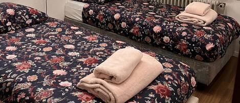 A room with two beds, each with a floral-patterned bedspread and matching pillows, and a radiator above one bed.