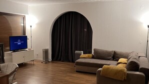 A modern living room with a flat-screen TV, a sofa, and a large arched window. - Beautiful 8 Bed Apartment in Hallenberg (Hallenberg)