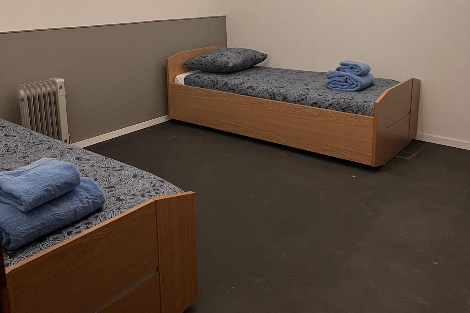 Een kleine kamer met een enkel bed, houten hoofdeinde en een grijze vloer.