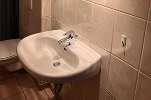 A bathroom with a white sink, a toilet, and beige tiled walls. - Beautiful 8 Bed Apartment in Hallenberg (Hallenberg)