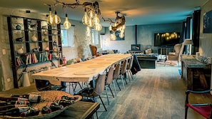 Un vaste espace dédié à la salle à manger, avec une longue table, de nombreuses chaises et des luminaires suspendus.