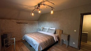 Un dormitorio con pared de piedra, cama con cabecera, mesitas de noche y una lámpara de techo con forma de rama.