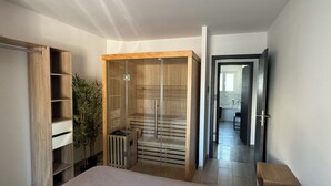 Makuuhuoneessa on sänky, puinen vaatekaappi, pieni puinen jakkara ja ruukussa oleva kasvi.
