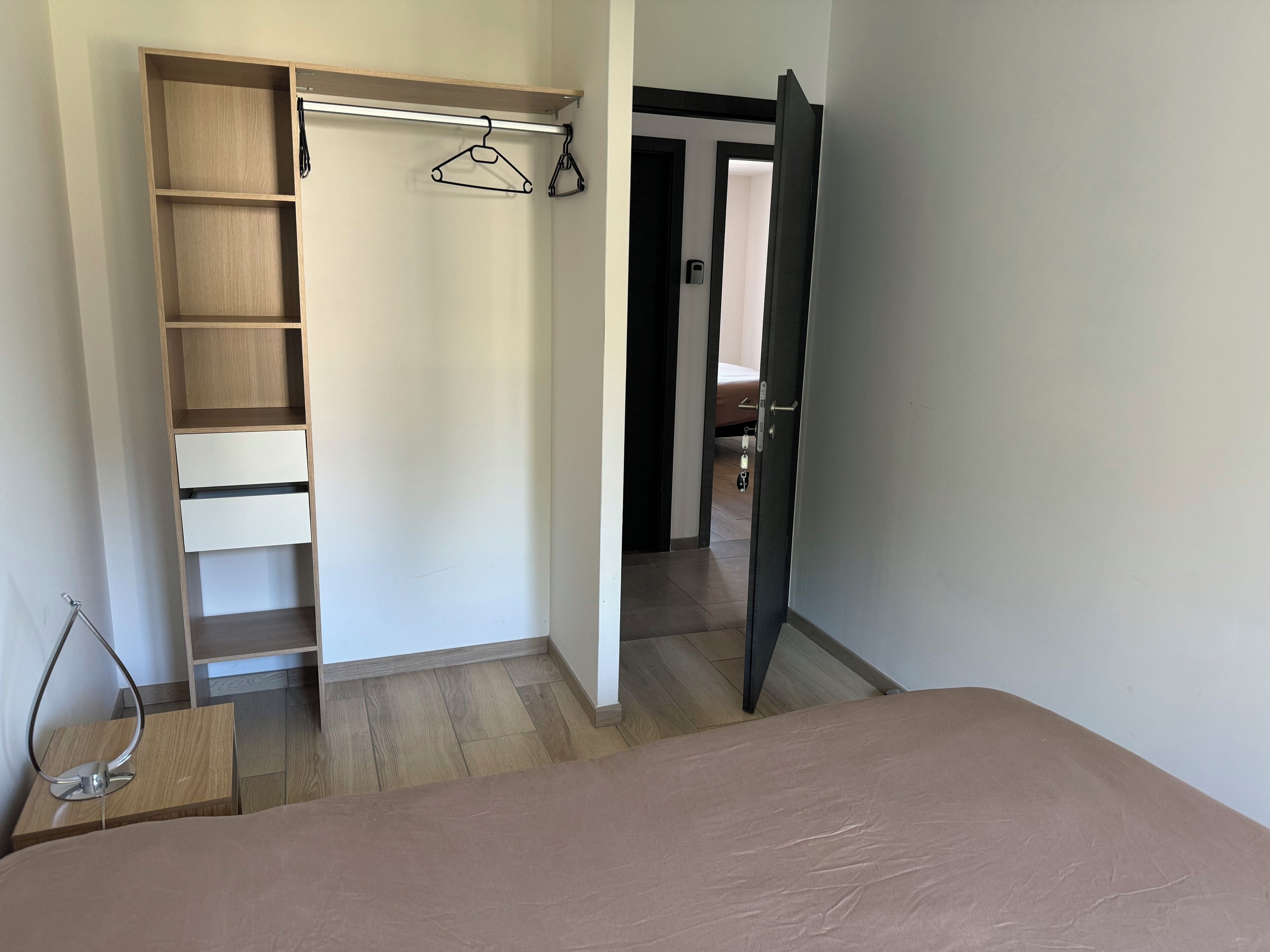 Un dormitorio con cama, un armario de madera con varios estantes y una puerta que da a otra habitación.
