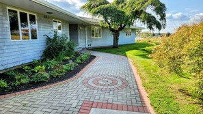 Una casa con un vialetto lastricato che conduce all'ingresso, circondata da un giardino curato e un grande albero.