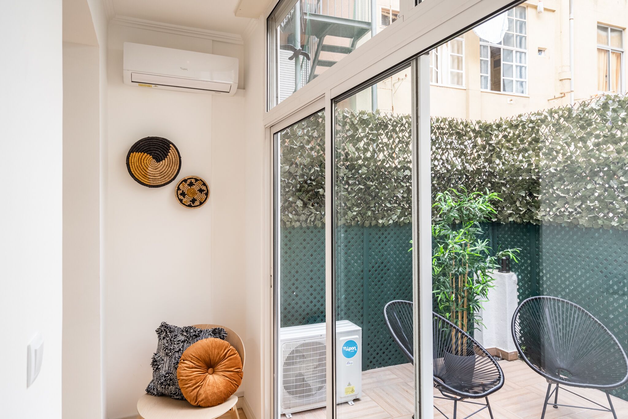 A modern living room with a glass door leading to a balcony, a white air conditioner, two black chairs, and a decorative pillow.